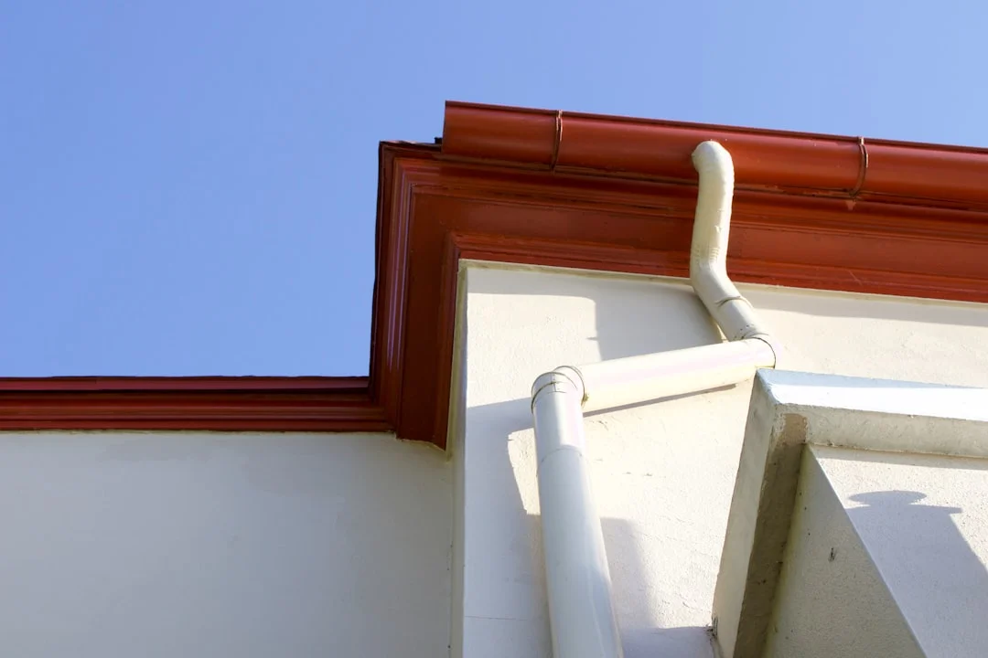 A craftsman installing a copper half-round gutter on a historic home, sunlight catching the warm patina of the metal against painted wood fascia